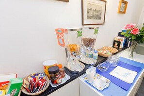 Una barra de desayuno con diversos alimentos y condimentos, una máquina de café y un florero con flores.