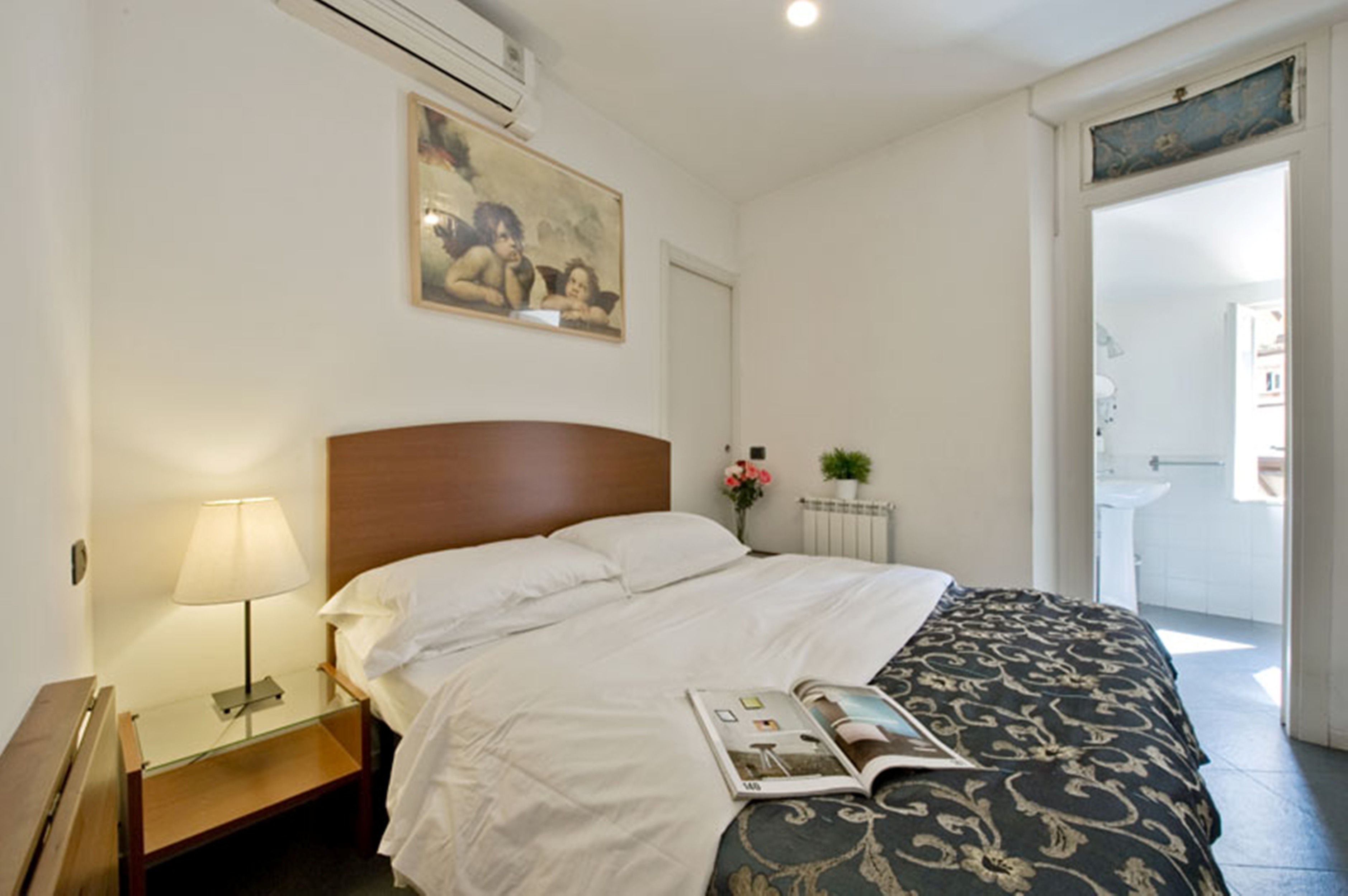 Une chambre d’hôtel avec un lit, une table de chevet avec une lampe, un tableau au mur et une vue sur la salle de bain.