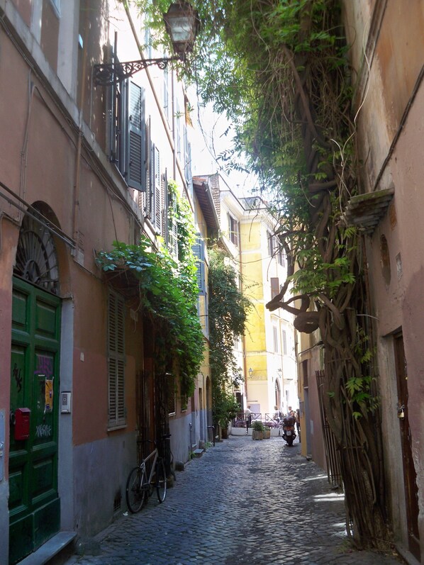 A narrow cobblestone street flanked by buildings with shutters and greenery. - Guest House Ventisei Scalini A Trastevere (Rome)