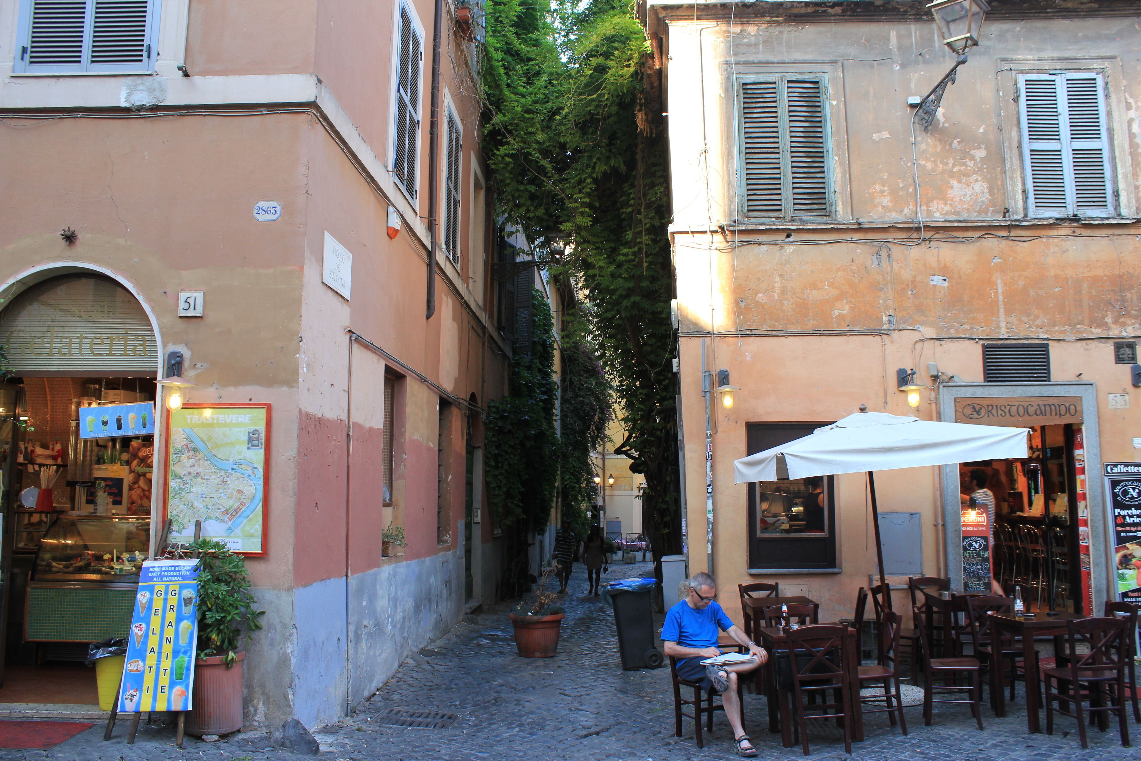 A narrow street with outdoor seating, a map, and a cafe.