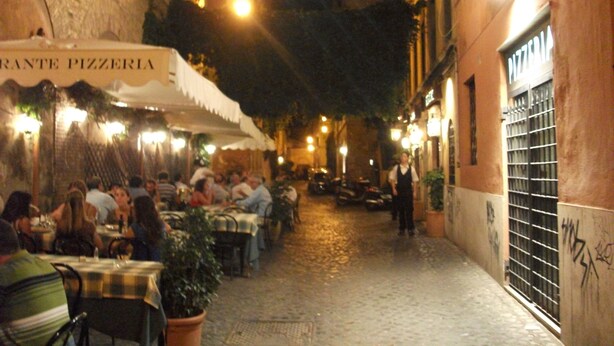 Una estrecha calle empedrada bordeada por mesas al aire libre de un restaurante.