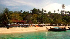 Une plage avec une eau turquoise et limpide, des palmiers et un bateau.