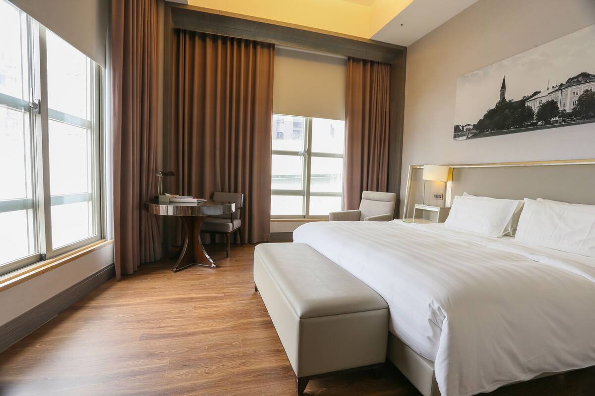 Ein Hotelzimmer mit einem großen Bett, einem Schreibtisch, einem Stuhl und einem fenster mit Vorhängen.