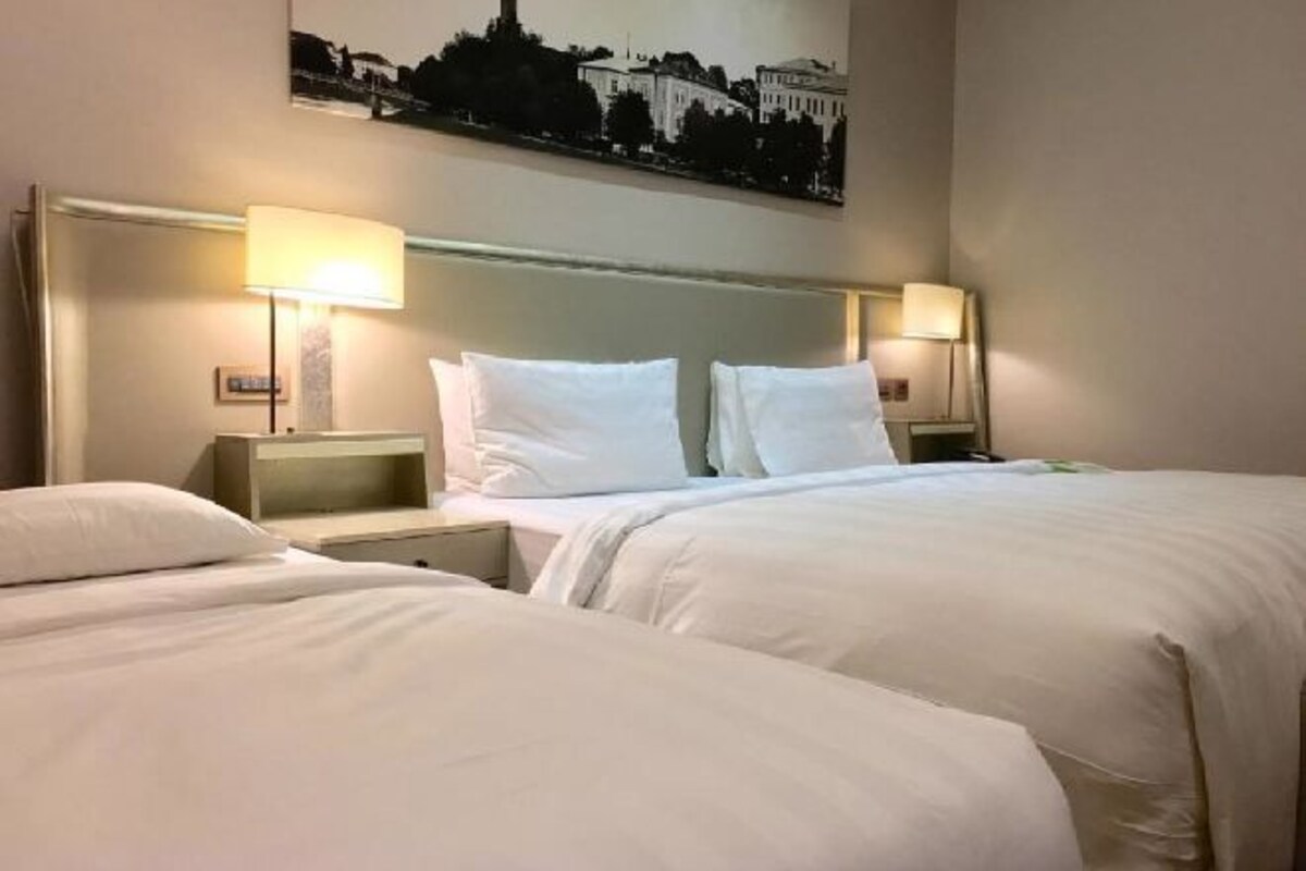 Een hotelkamer met twee bedden, nachtkastjes, lampen en een stadsgezicht schilderij aan de muur.