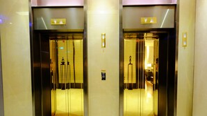 Two elevator doors with a metallic finish and a control panel on the wall.