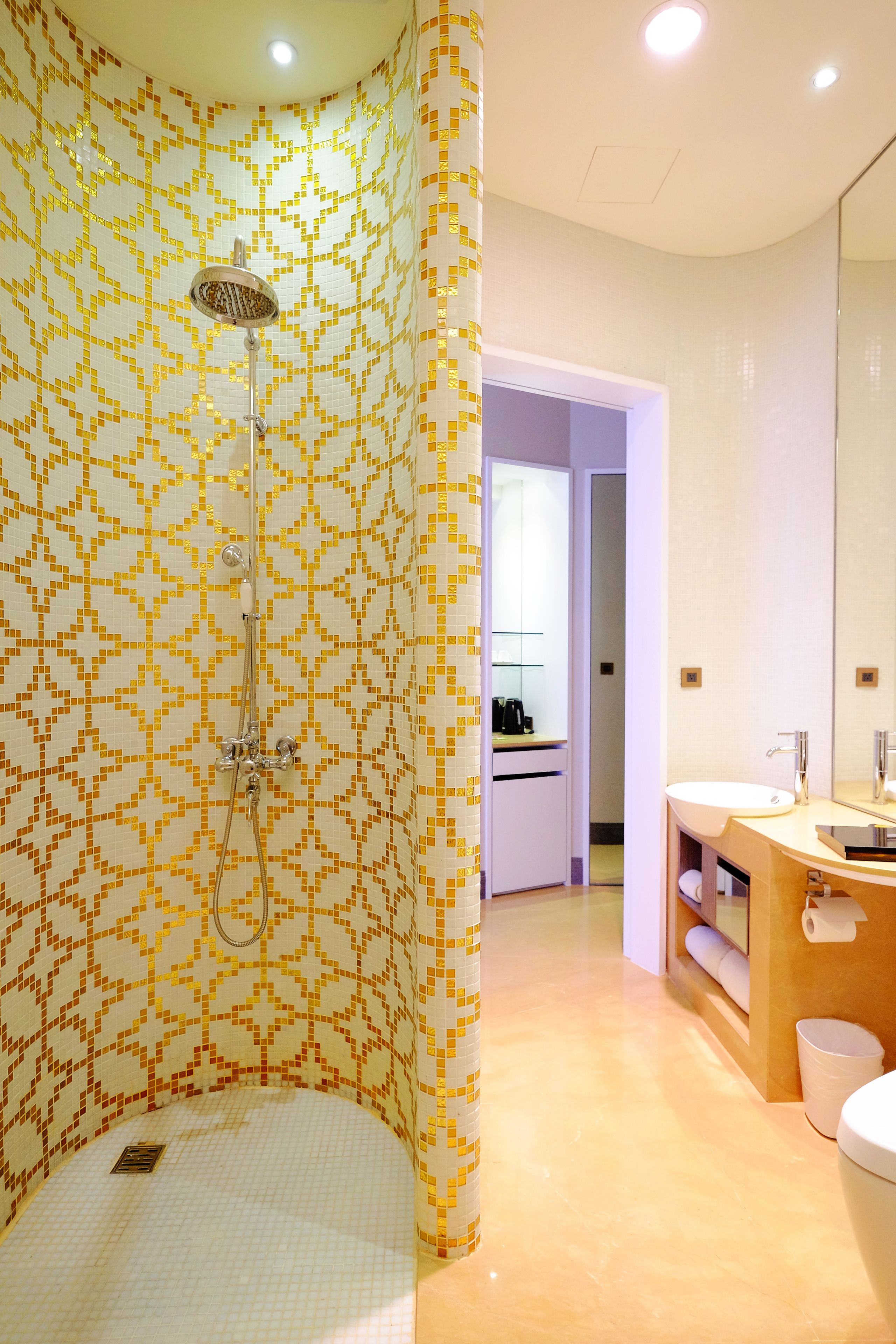 A modern bathroom with a patterned tile wall, a shower, a sink, and a toilet.
