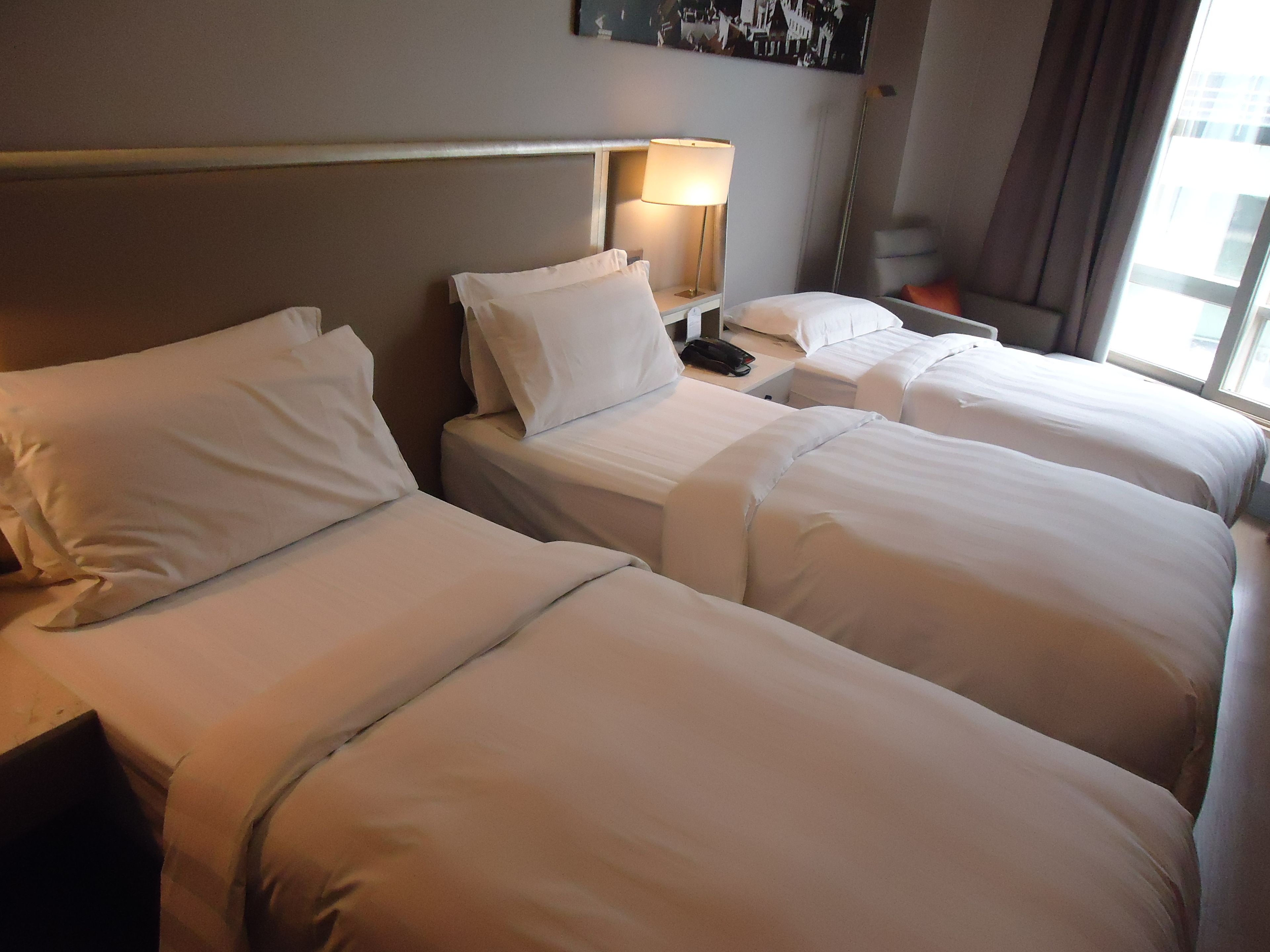 A hotel room with three single beds, a bedside lamp, and a nightstand with a phone.