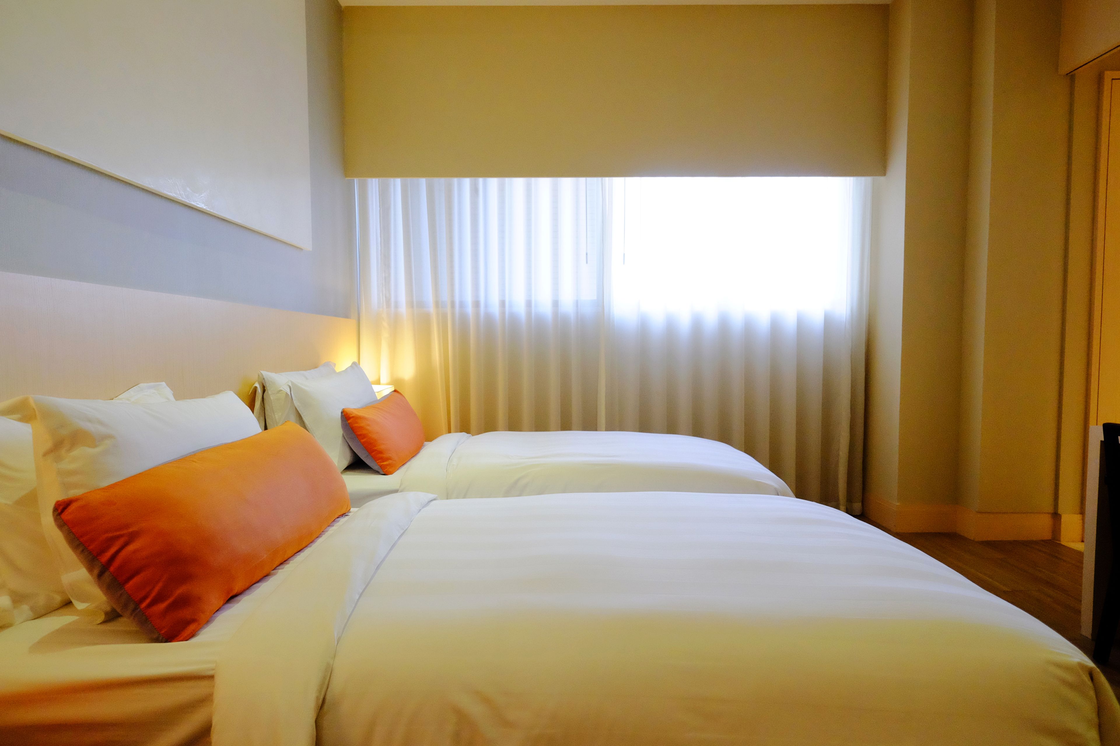 A hotel room with two beds, a large window with curtains, and a television on the right side.