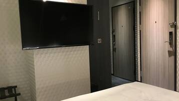 Ein Hotelzimmer mit Bett, Flachbildfernseher an der Wand, einer Tür und einer Wand mit geometrischem Muster.
