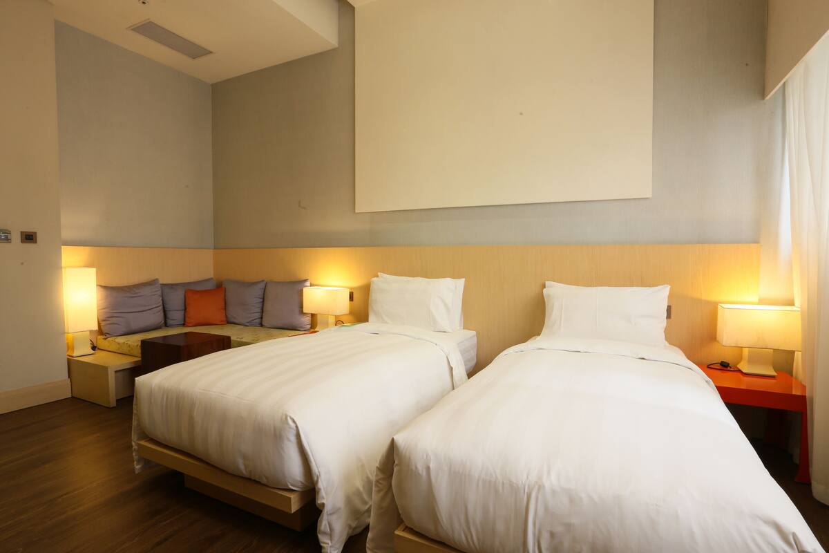 Ein Hotelzimmer mit zwei Betten, einem großen Wandfernseher und Nachttischlampen.