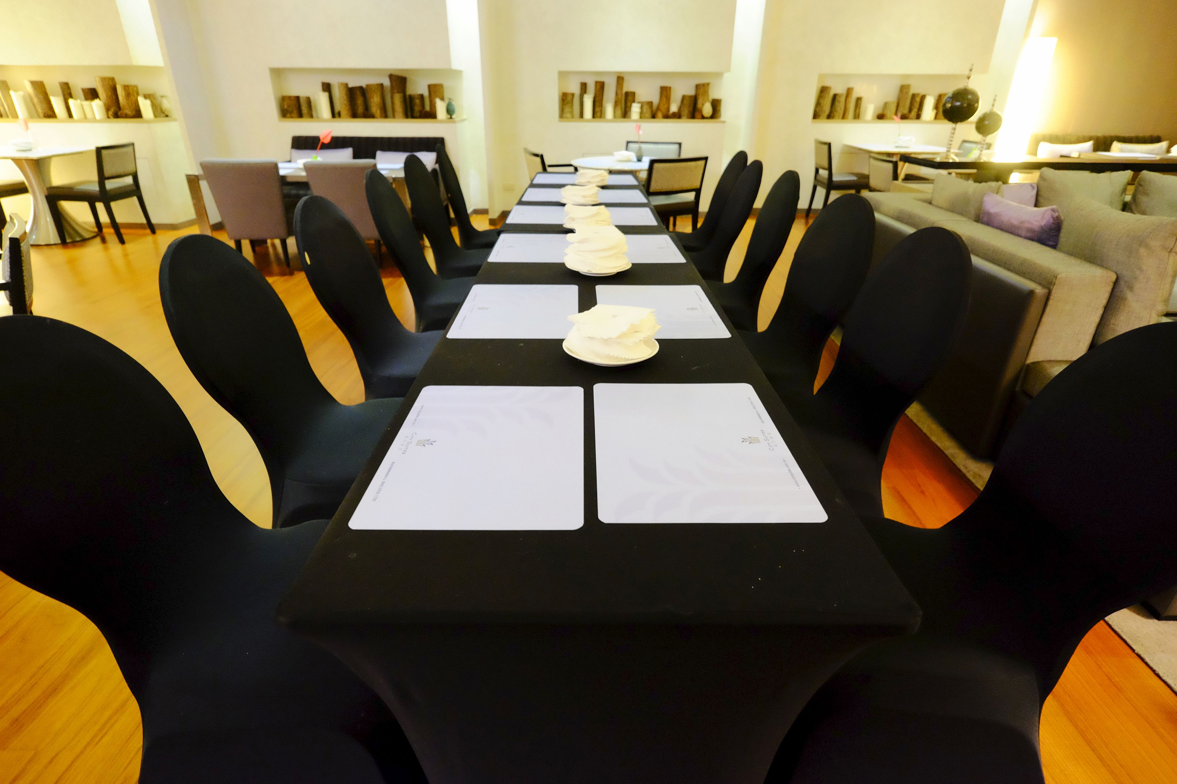 Ein Konferenzraum mit einem langen Tisch, schwarzen Stühlen und weißen Tischsets.