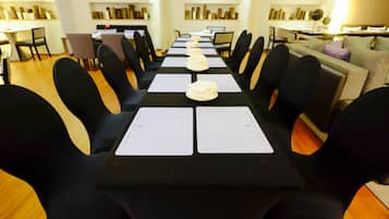 Ein Konferenzraum mit einem langen Tisch, schwarzen Stühlen und weißen Tischsets.