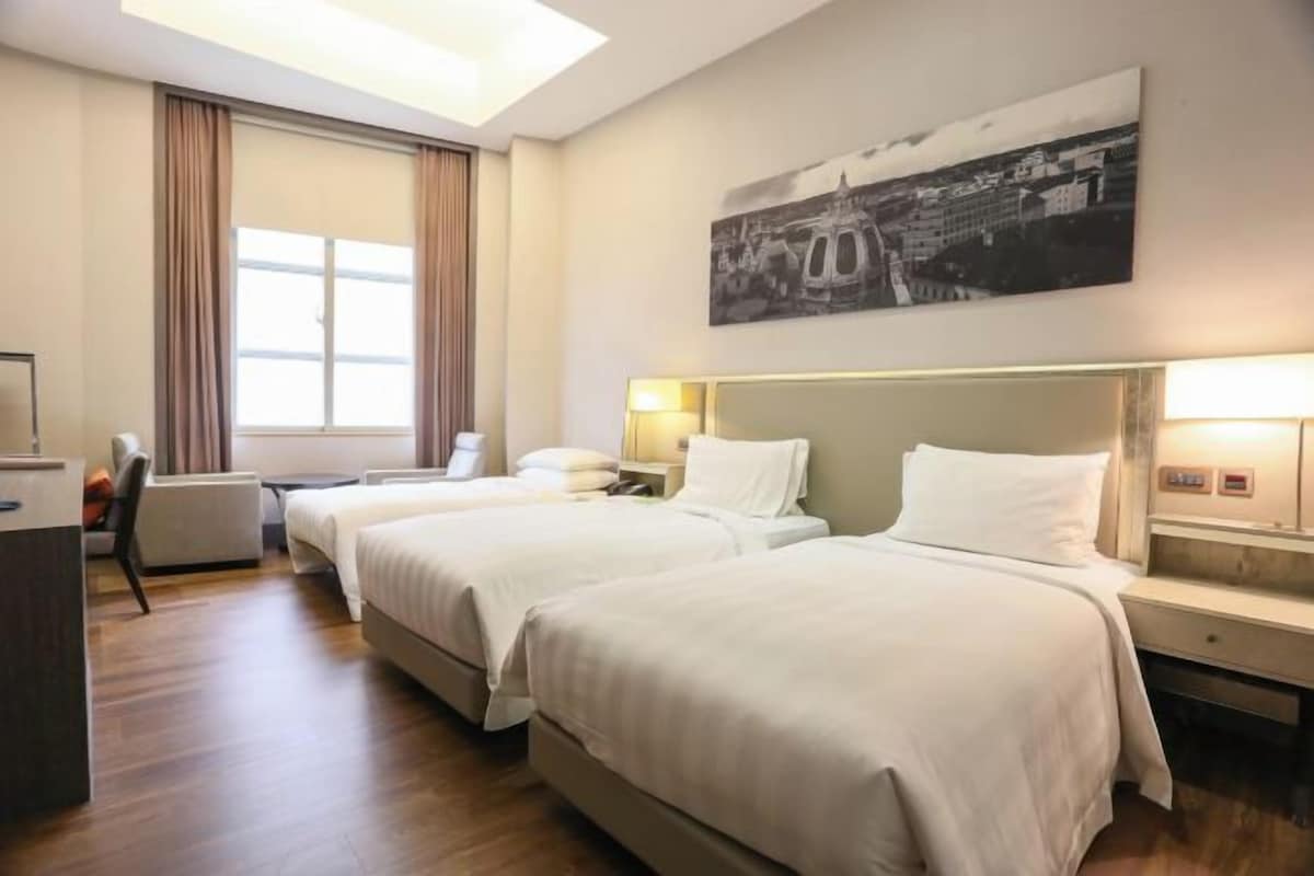 A hotel room with two beds, a desk, a chair, and a large window with curtains.
