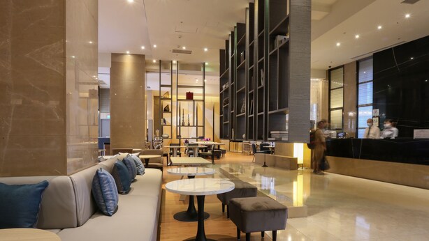 A modern lobby with a seating area, tables, and a reception desk.