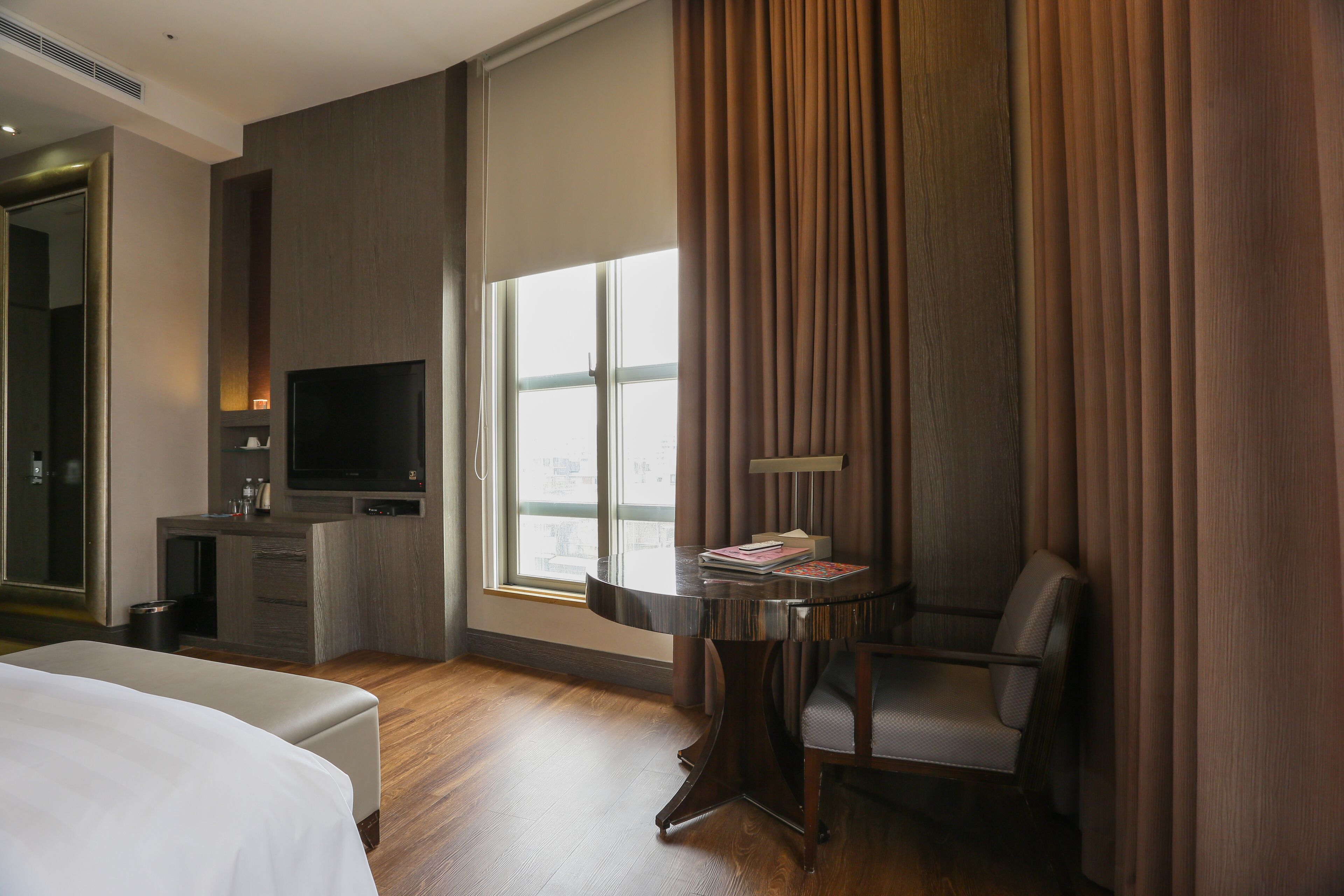 Une chambre d’hôtel avec un lit, un bureau avec une télévision, une chaise et une fenêtre avec des rideaux.