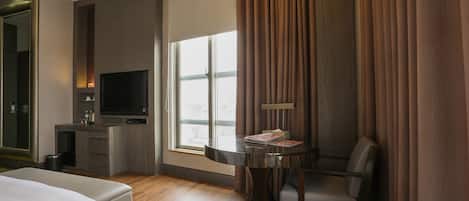 Une chambre d’hôtel avec un lit, un bureau avec une télévision, une chaise et une fenêtre avec des rideaux.