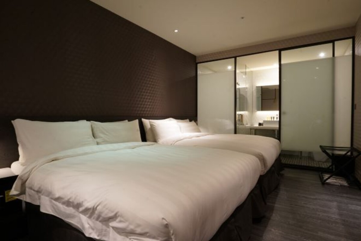 A modern hotel room with a large bed, a separate seating area, and a glass partition.