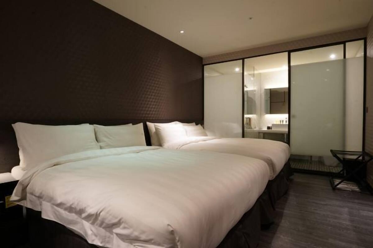 Ein modernes Hotelzimmer mit einem großen Bett, einer separaten Sitzecke und einer Glastrennwand.