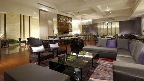 A spacious lobby with a modern design, featuring a mix of seating areas, a reception desk, and a decorative wall.