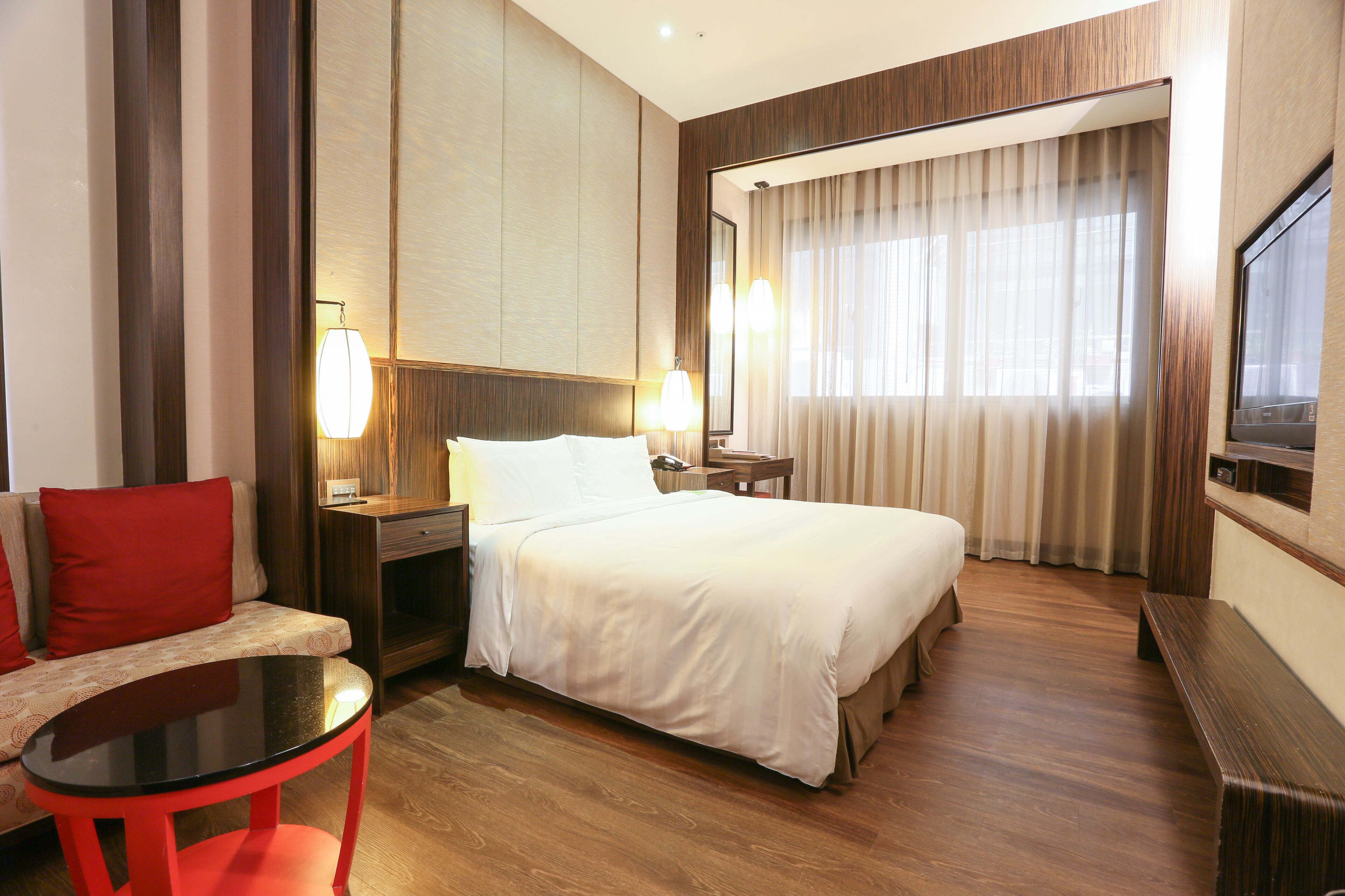 Une chambre d’hôtel avec un lit, un canapé, une petite table, une télévision et un miroir.