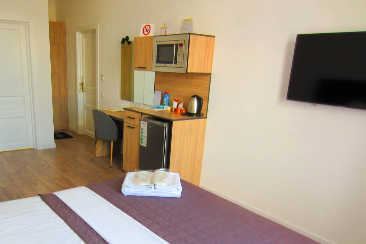 A hotel room with a bed, a desk with a microwave, a refrigerator, and a TV on the wall.