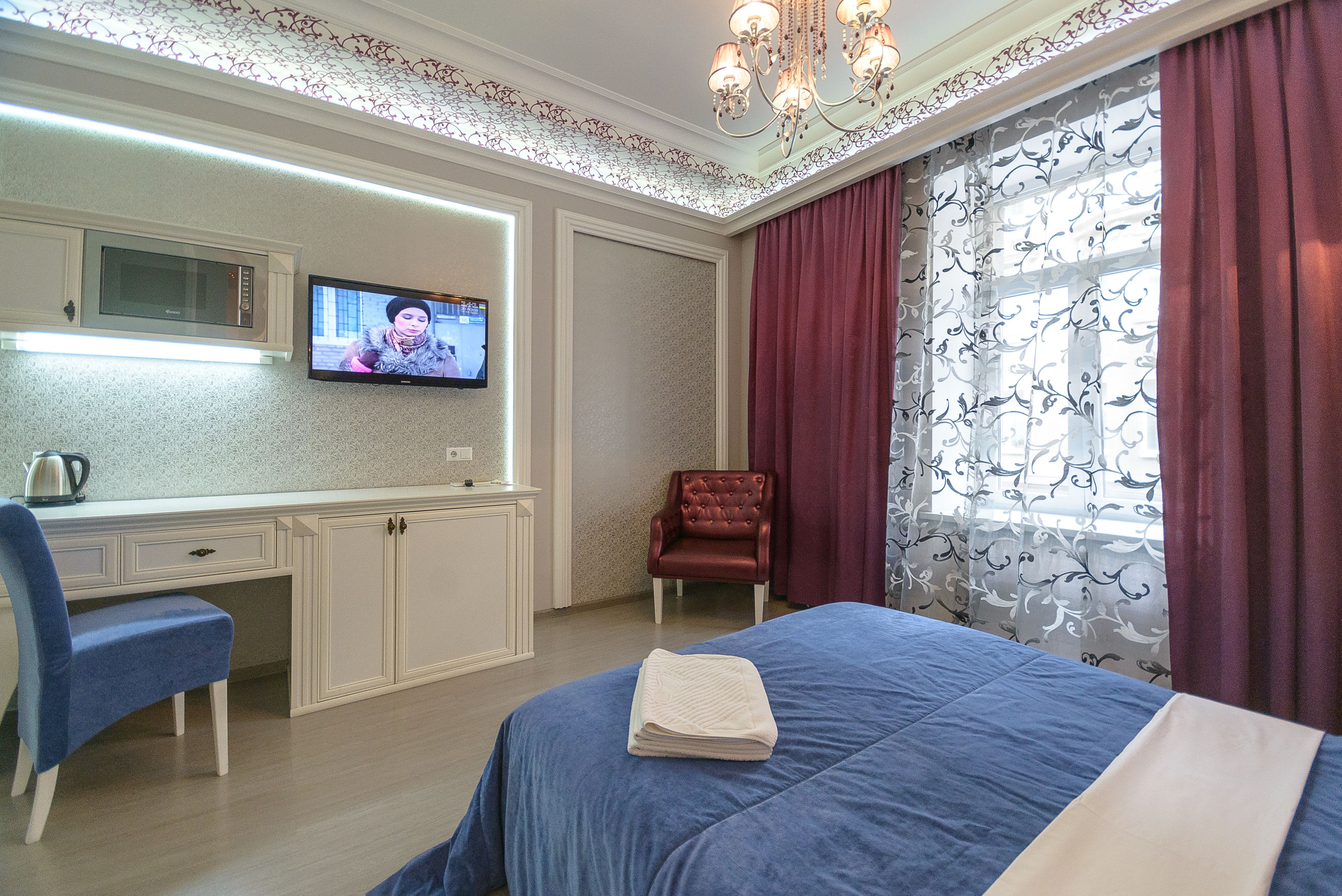 Habitación de hotel con cama, escritorio, silla, televisor y ventana con cortinas.