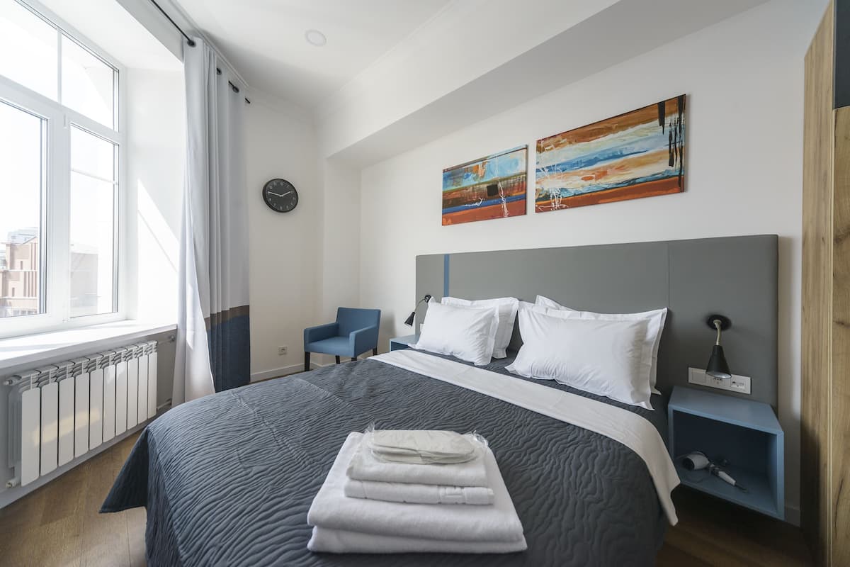 A hotel room with a large bed, a nightstand, a chair, and artwork on the wall.