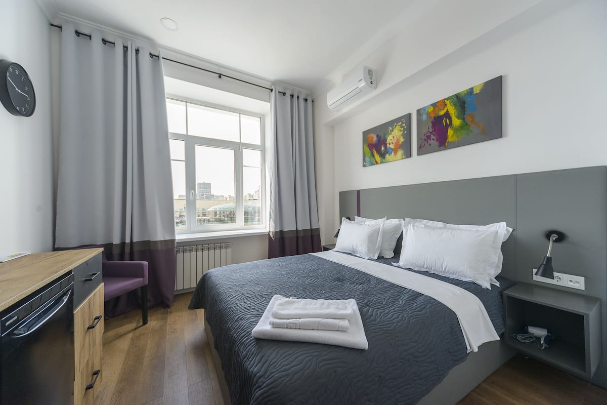 A modern hotel room with a large bed, a desk, and a view of the city.