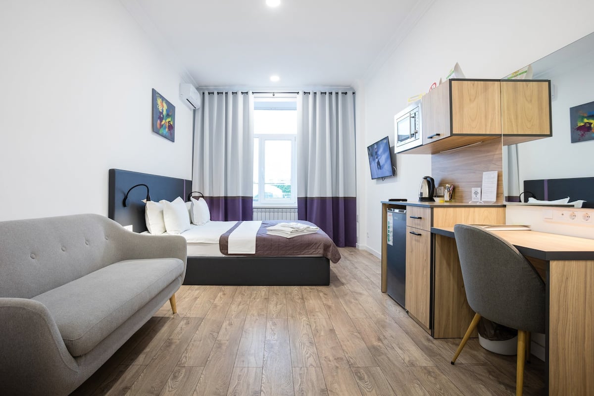 A modern hotel room with a bed, a sofa, a desk, and a television.