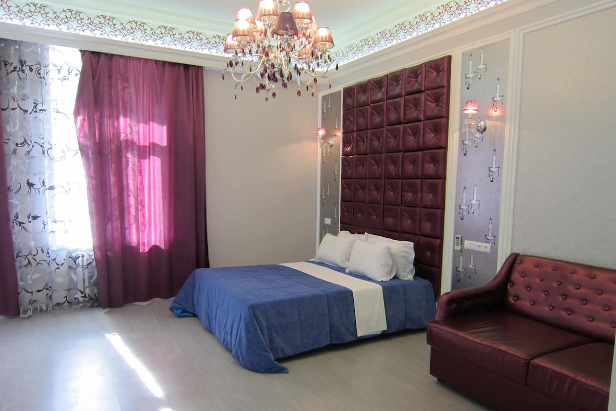 A bedroom with a bed, a red sofa, and a chandelier.