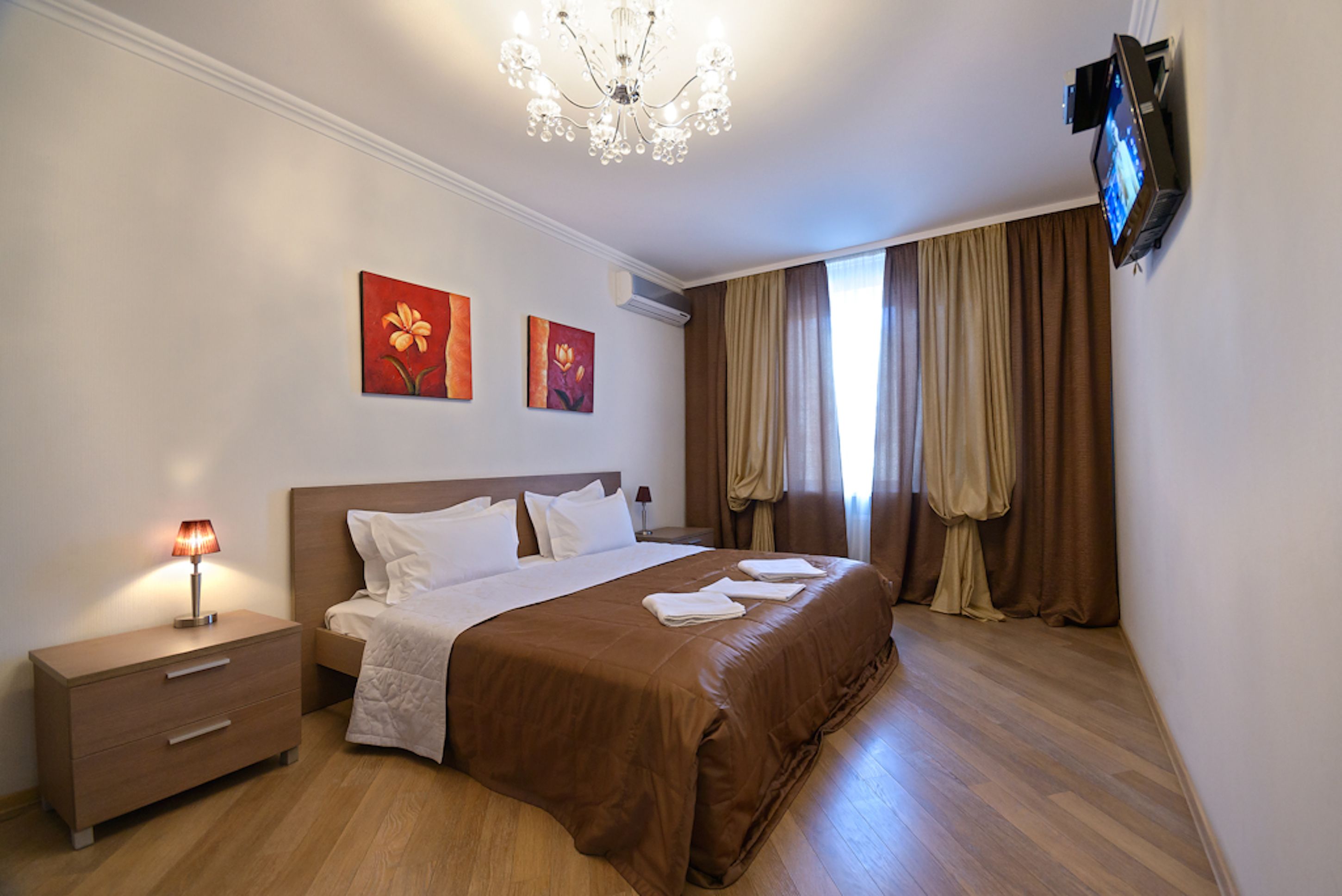 Habitación de hotel con una cama grande, una mesita de noche con lámpara, un televisor de pantalla plana en la pared y dos cuadros colgados.