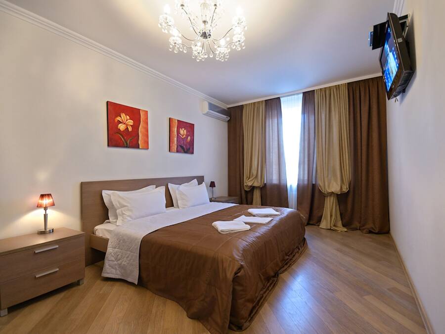 Habitación de hotel con una cama grande, una mesita de noche con lámpara, un televisor de pantalla plana en la pared y dos cuadros colgados.