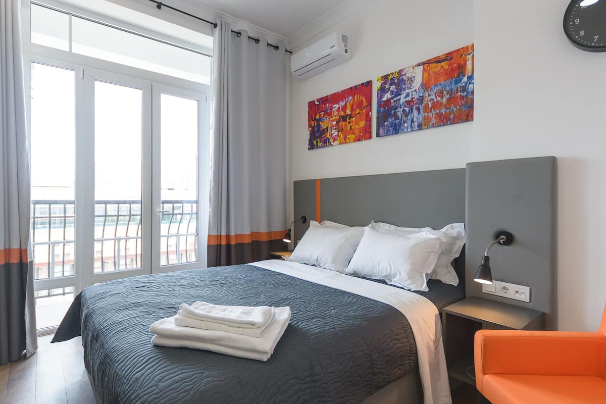 A hotel room with a bed, a nightstand, a chair, and a balcony view.