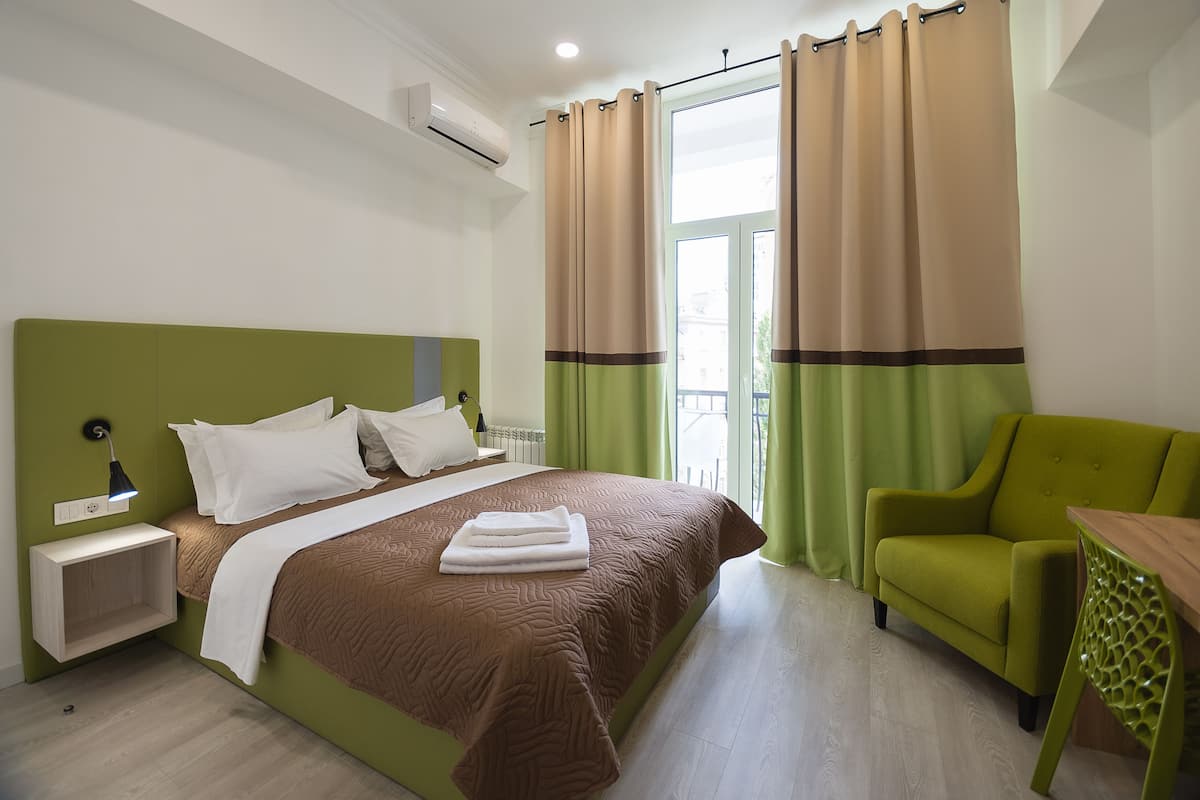 A modern hotel room with a green headboard, a neatly made bed, a green armchair, and a wooden table.