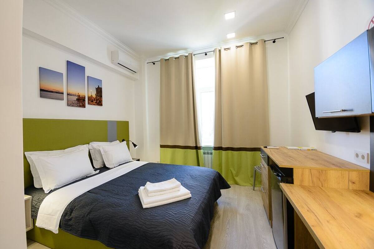 A hotel room with a bed, a desk, a TV, and a window with curtains.