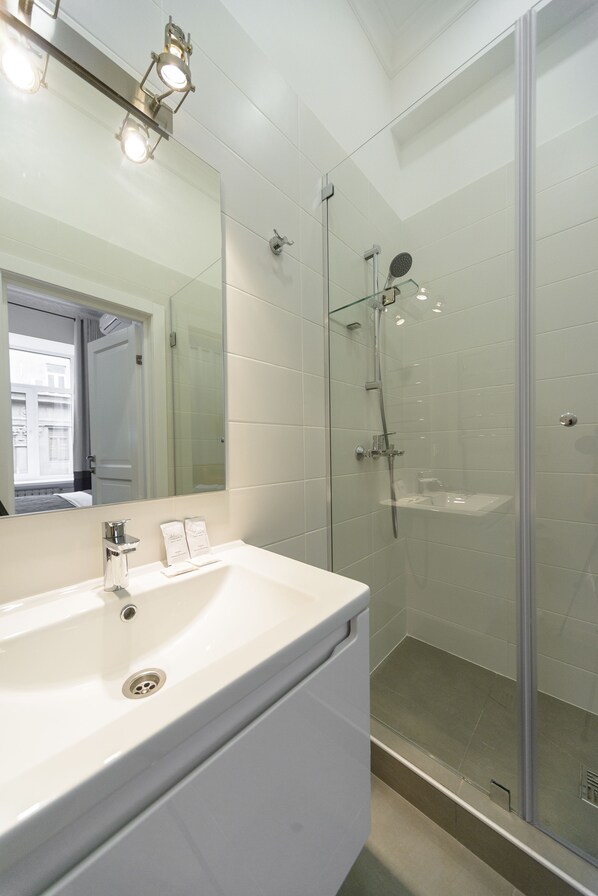 A modern bathroom with a glass-enclosed shower, a large mirror, and a white sink.