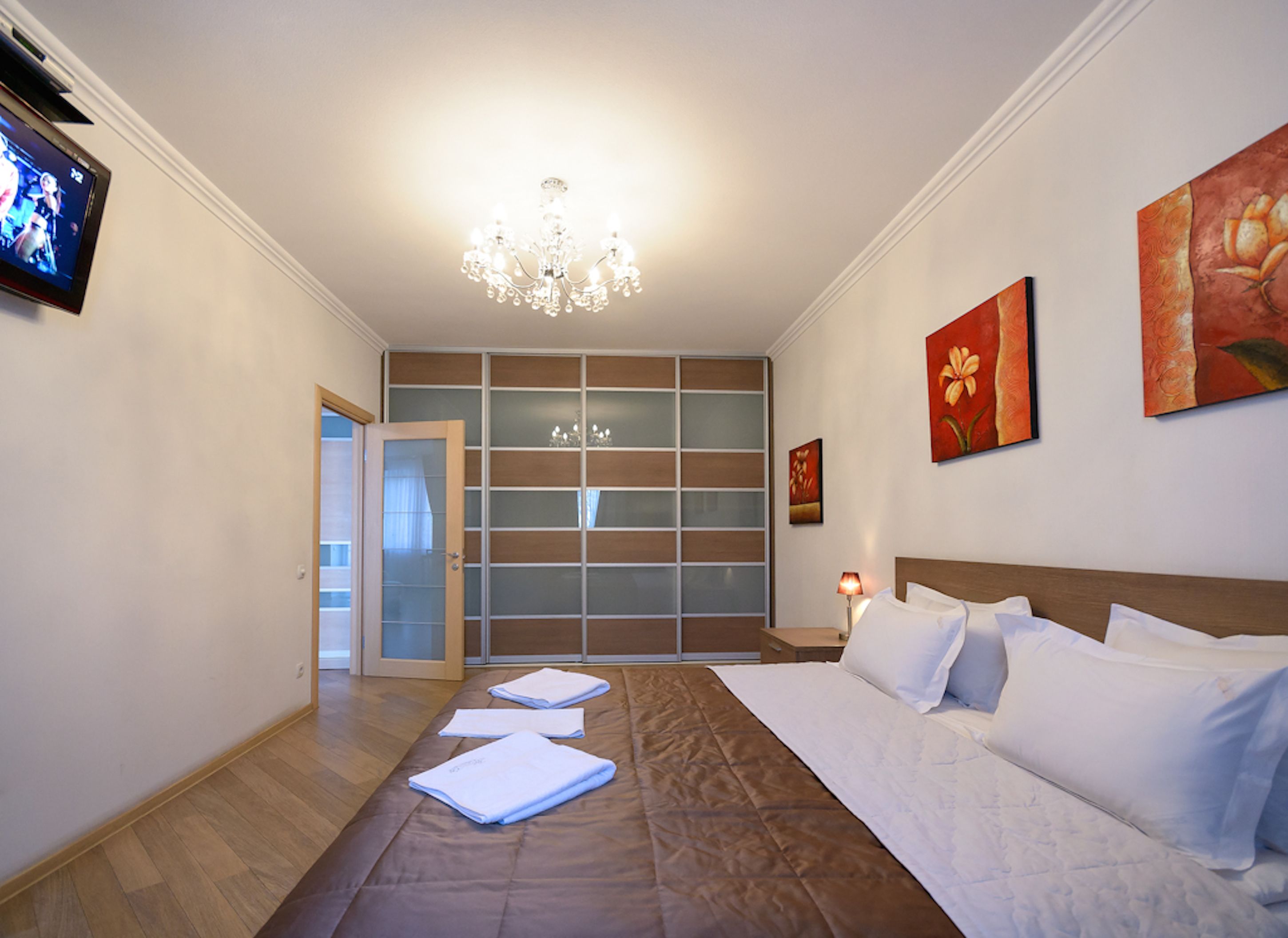 A hotel room with a large bed, a wardrobe with sliding doors, a chandelier, and artwork on the walls.