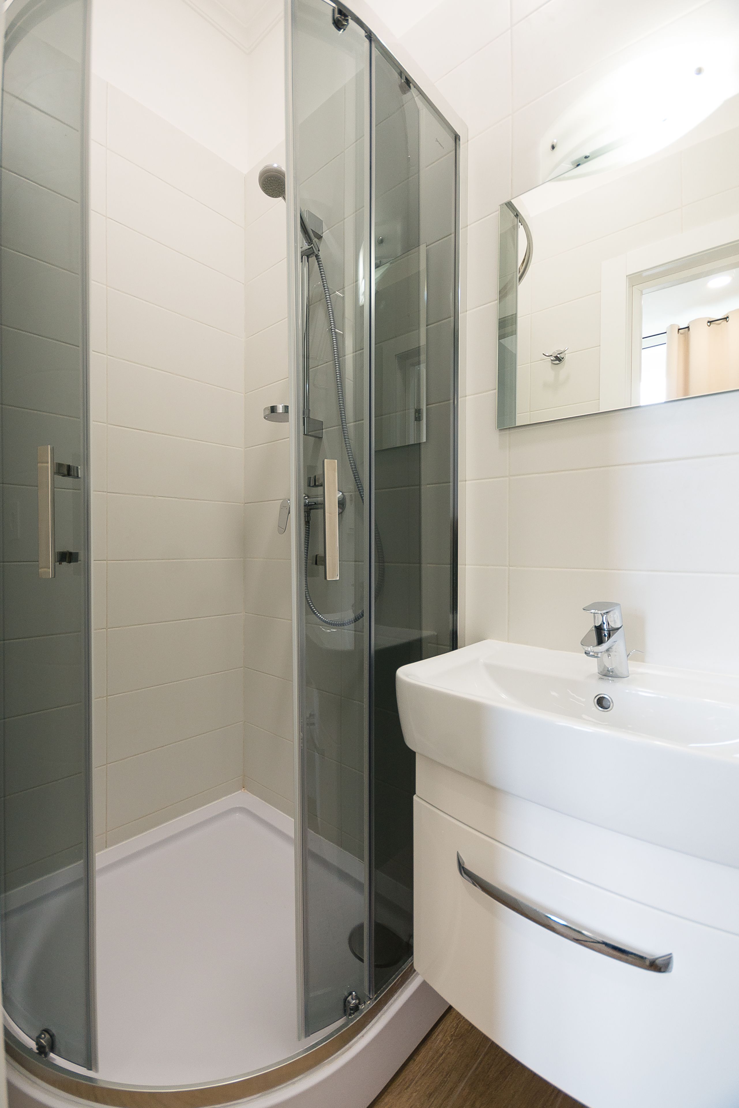 Un baño moderno con cabina de ducha de vidrio, un lavamanos blanco y un espejo sobre él.