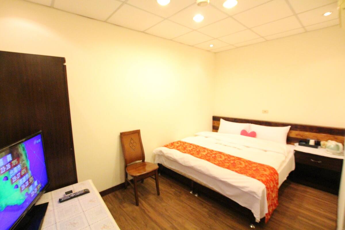 Een hotelkamer met een bed, een stoel, een bureau met een afstandsbediening en een televisie.
