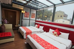 A hotel room with two beds, a sofa, and a window with a city view.
