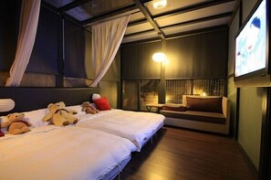 A hotel room with two beds, a TV, a bedside table, and a window with curtains.