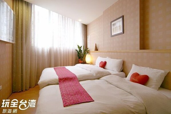 A hotel room with two beds, beige walls, a framed picture, and a window with curtains.
