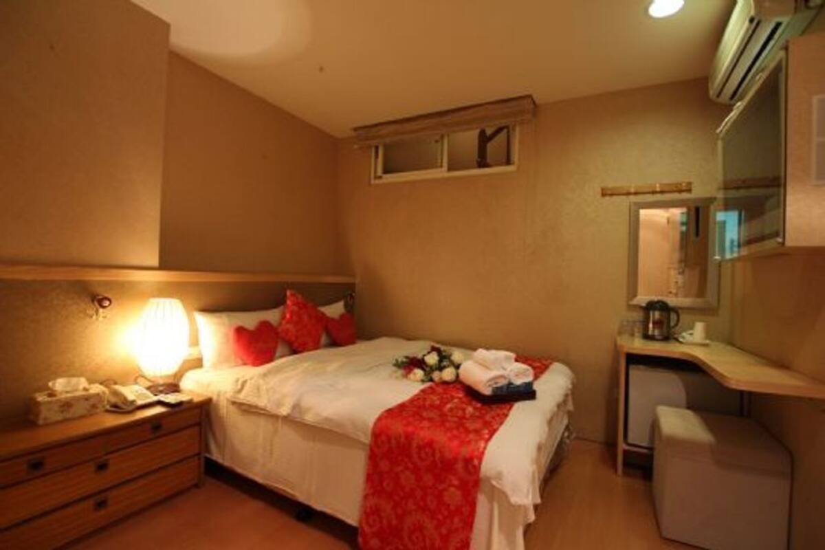 Een hotelkamer met een bed, nachtkastje, lamp en een klein bureau met stoel.