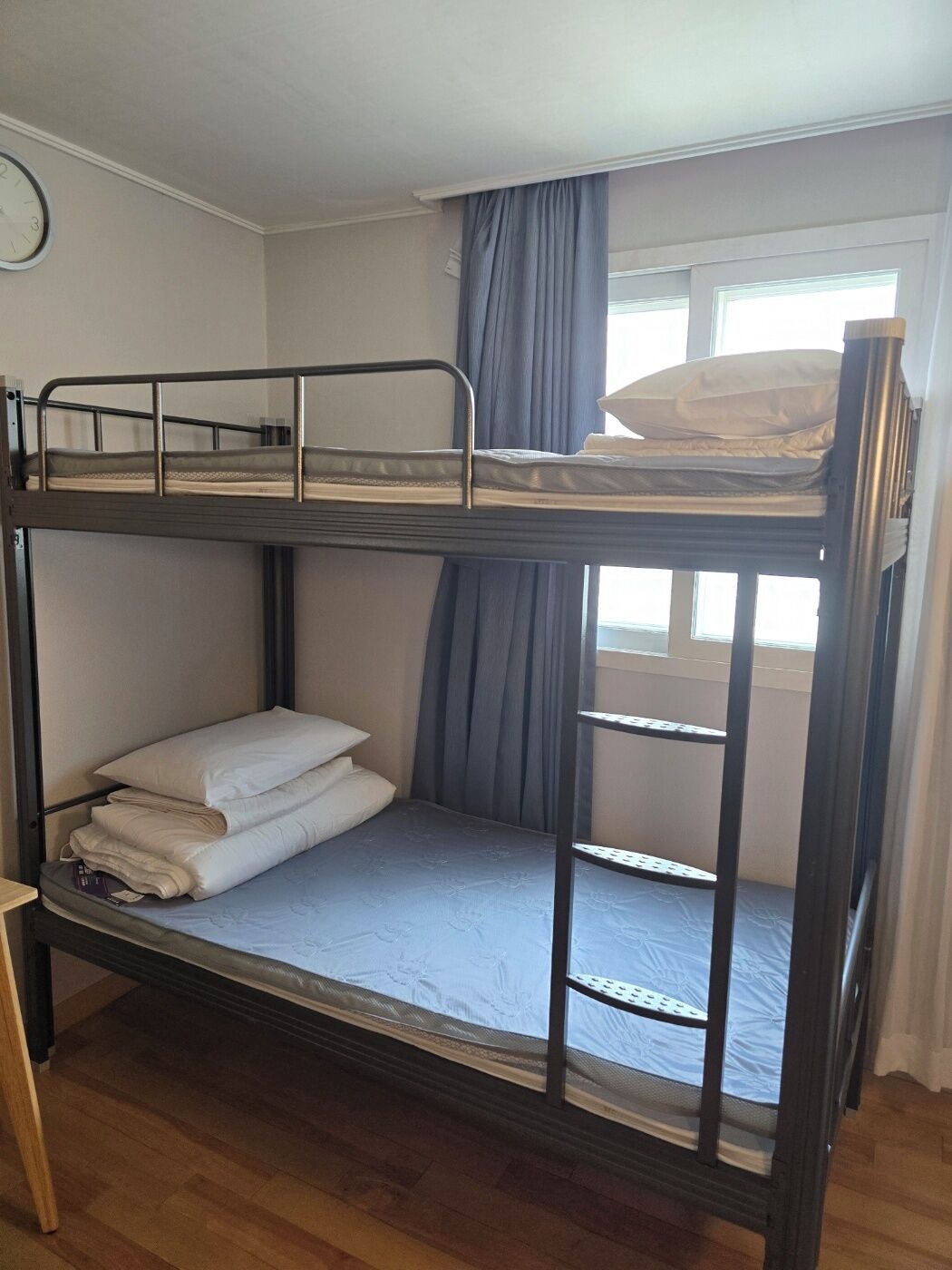 Une chambre avec un lit superposé, une fenêtre, des rideaux et une horloge au mur.