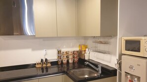 A kitchen with beige cabinets, a black countertop, a stainless steel range hood, a sink, and a microwave.