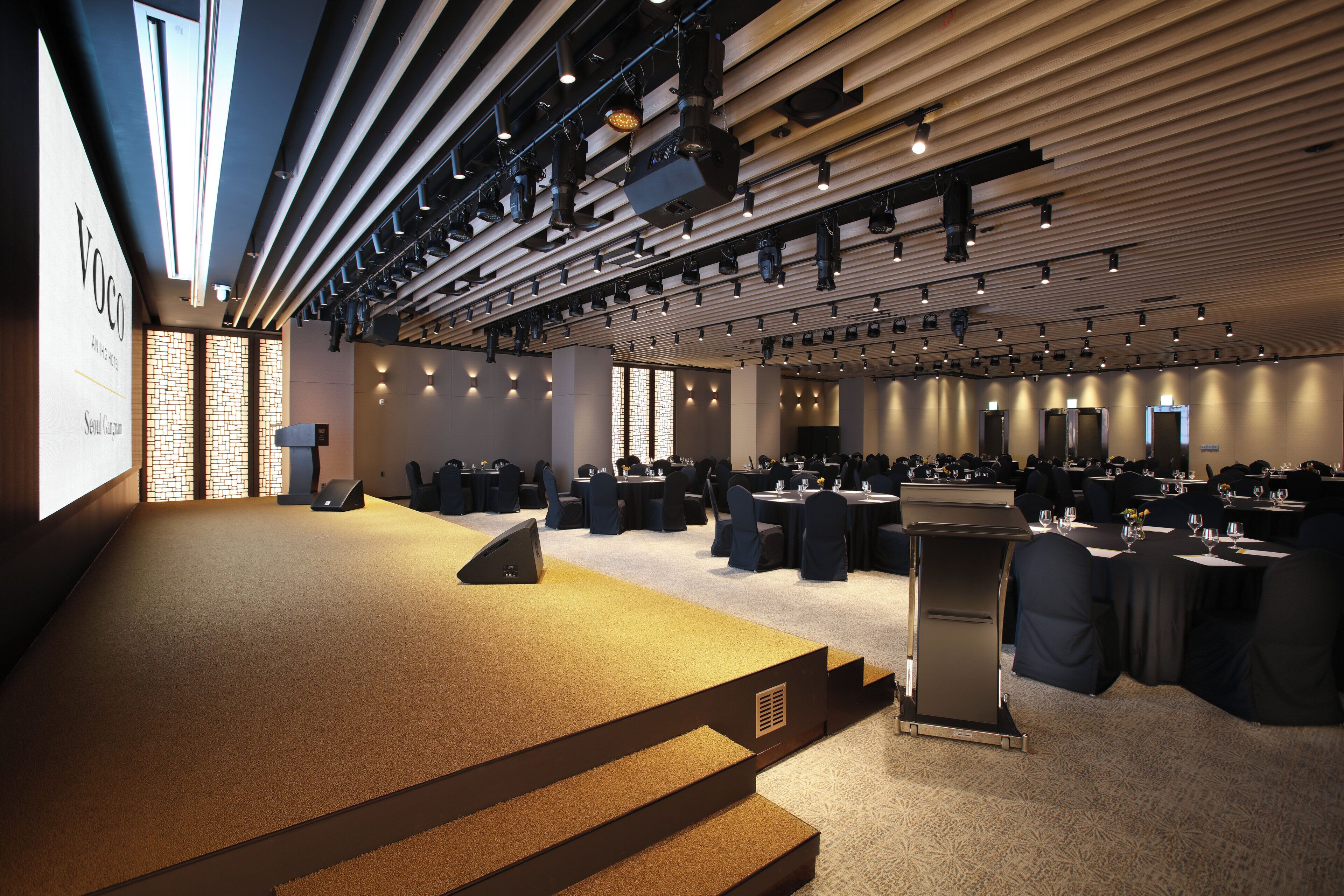 Un salón de conferencias con un escenario, filas de mesas y sillas.