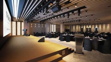Un salón de conferencias con un escenario, filas de mesas y sillas.