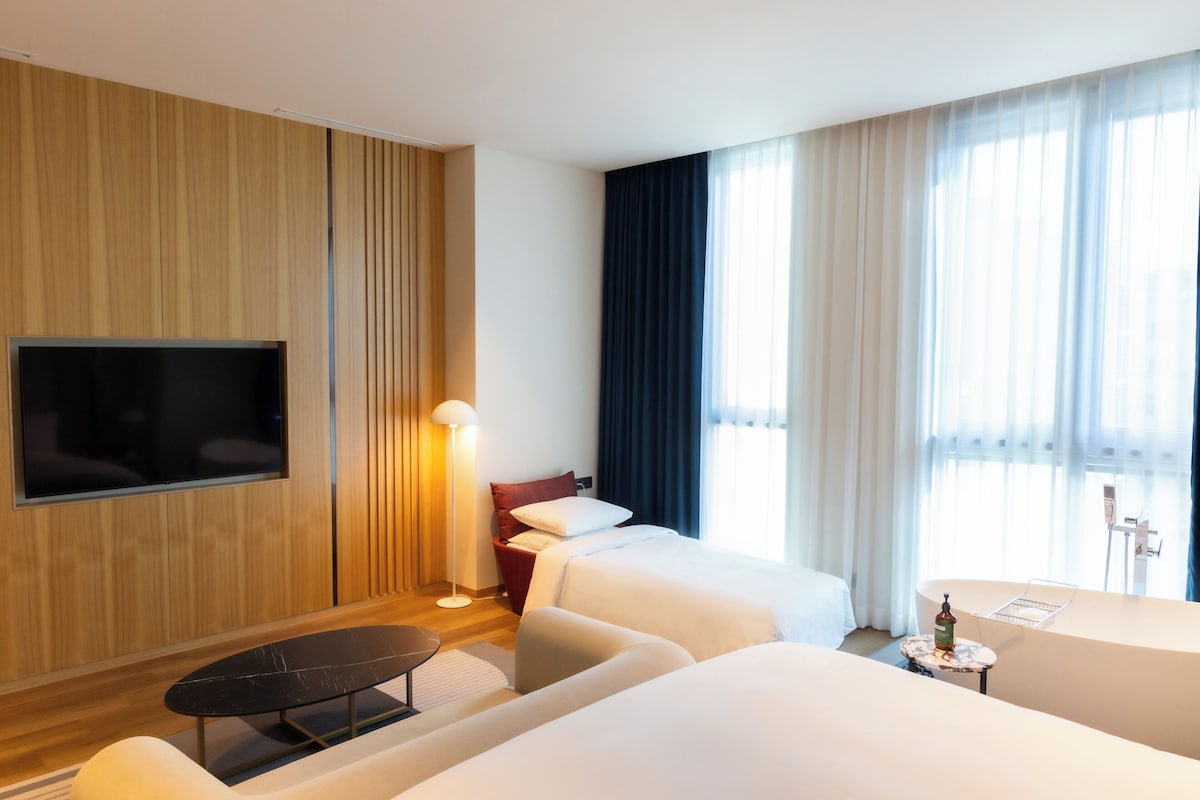 A hotel room with a TV, two beds, a sofa, a small table, and a lamp.