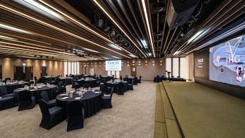 A conference room with multiple tables, chairs, and a large screen displaying 'Voco by IHG Seoul Gangnam'.