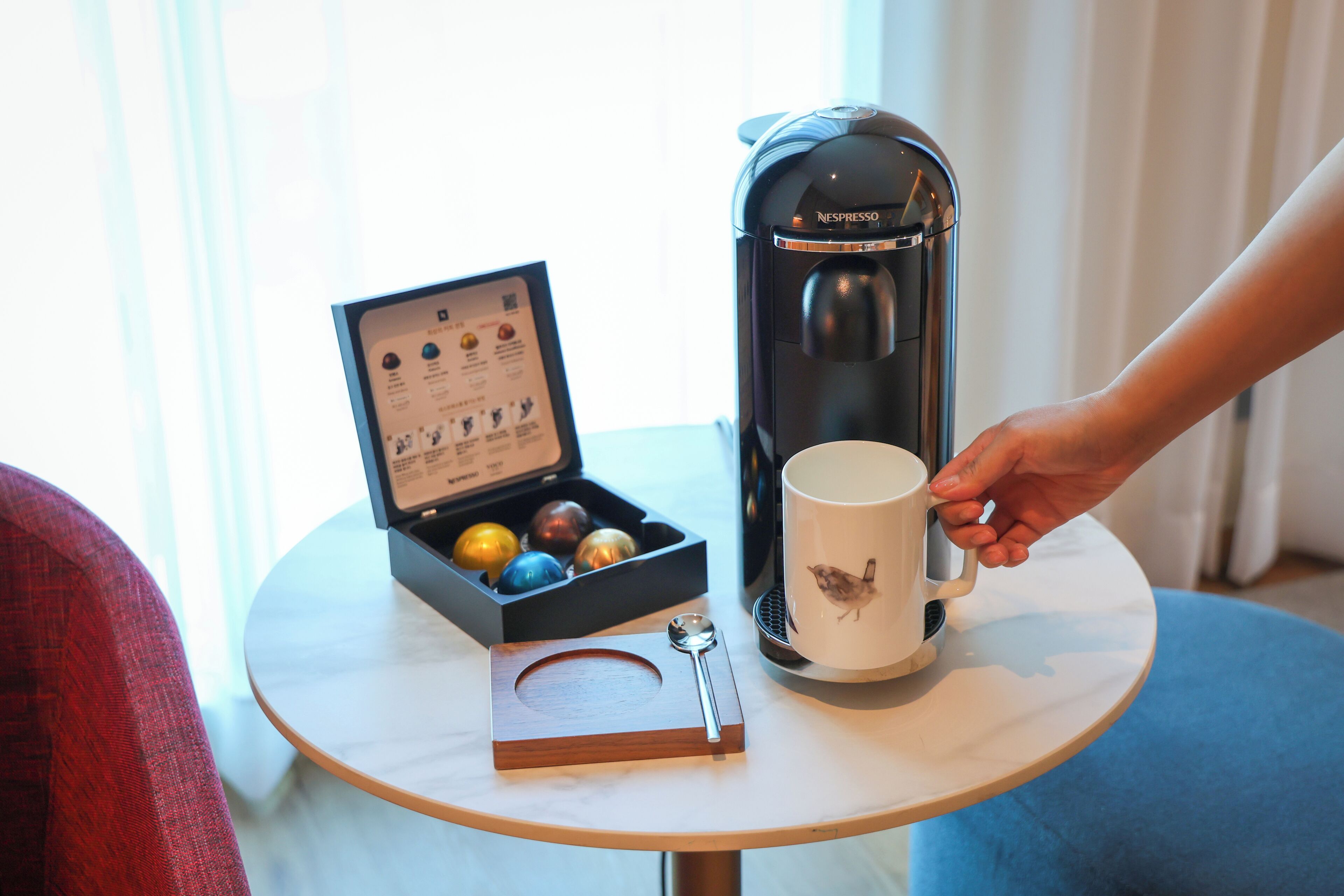 A coffee maker on a table with a mug and a box of chocolates.